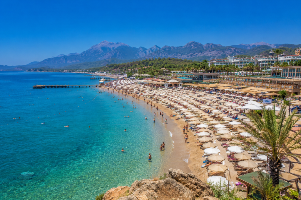 Antalya beach in July – turquoise Mediterranean sea, golden sandy beach with sunbeds and umbrellas, Taurus Mountains in the background