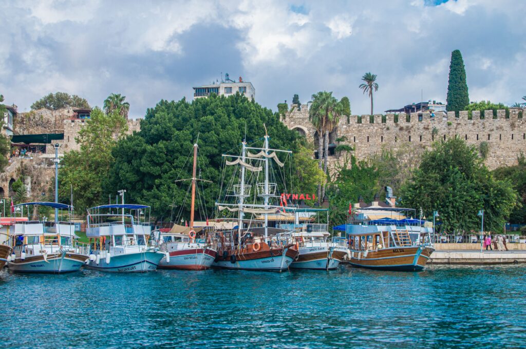 Boats docked near an ancient stone fortress with lush greenery in Antalya