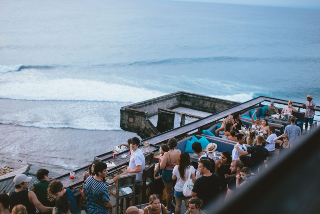 Lively outdoor bar scene by the ocean with crowd enjoying drinks