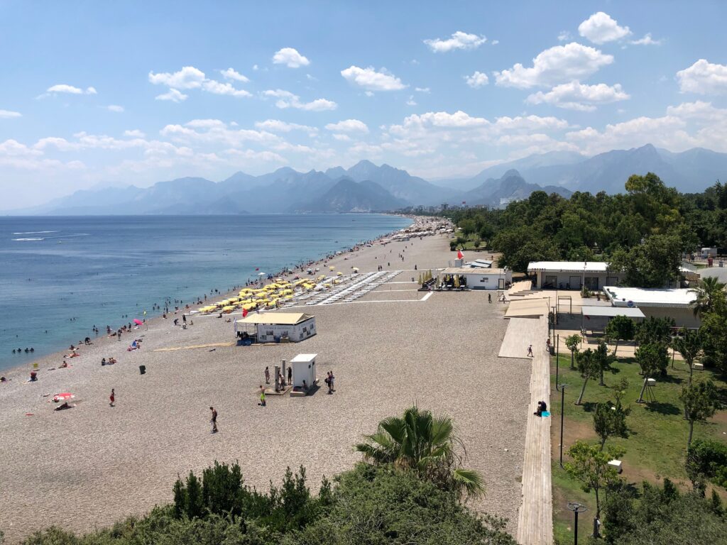 People relaxing on a sandy beach with mountains near Lara Beach, Antalya