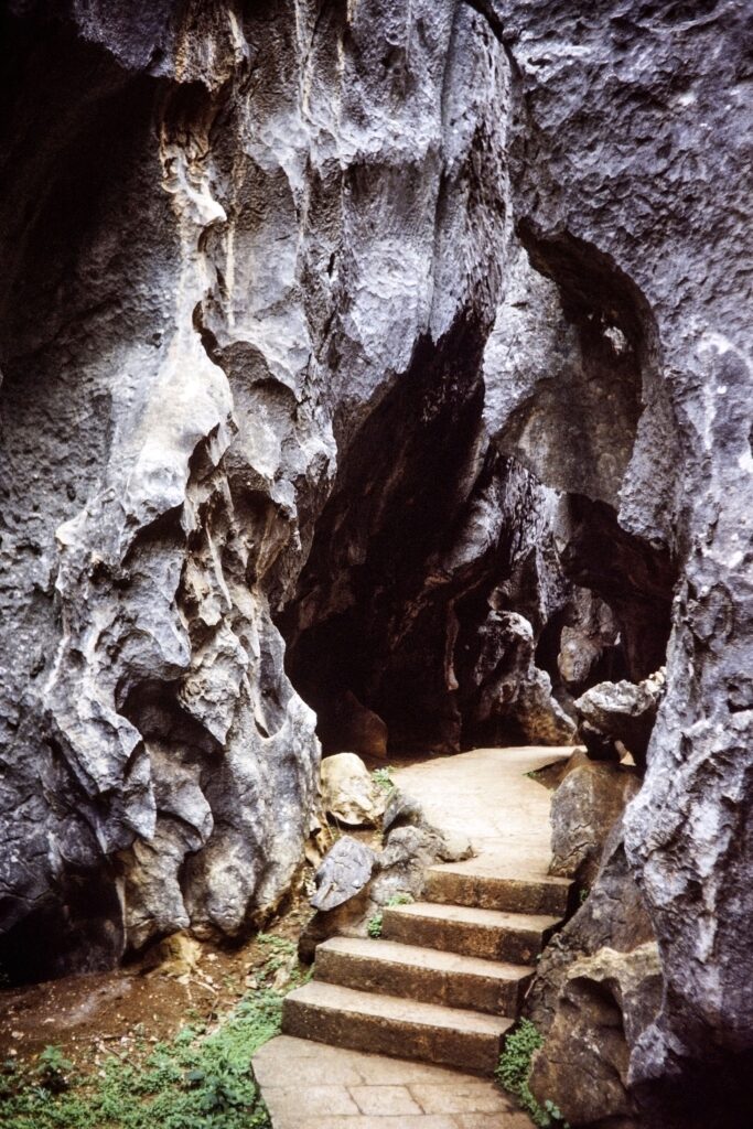 A natural limestone cave entrance reached by steps, similar to Karain Cave near Antalya