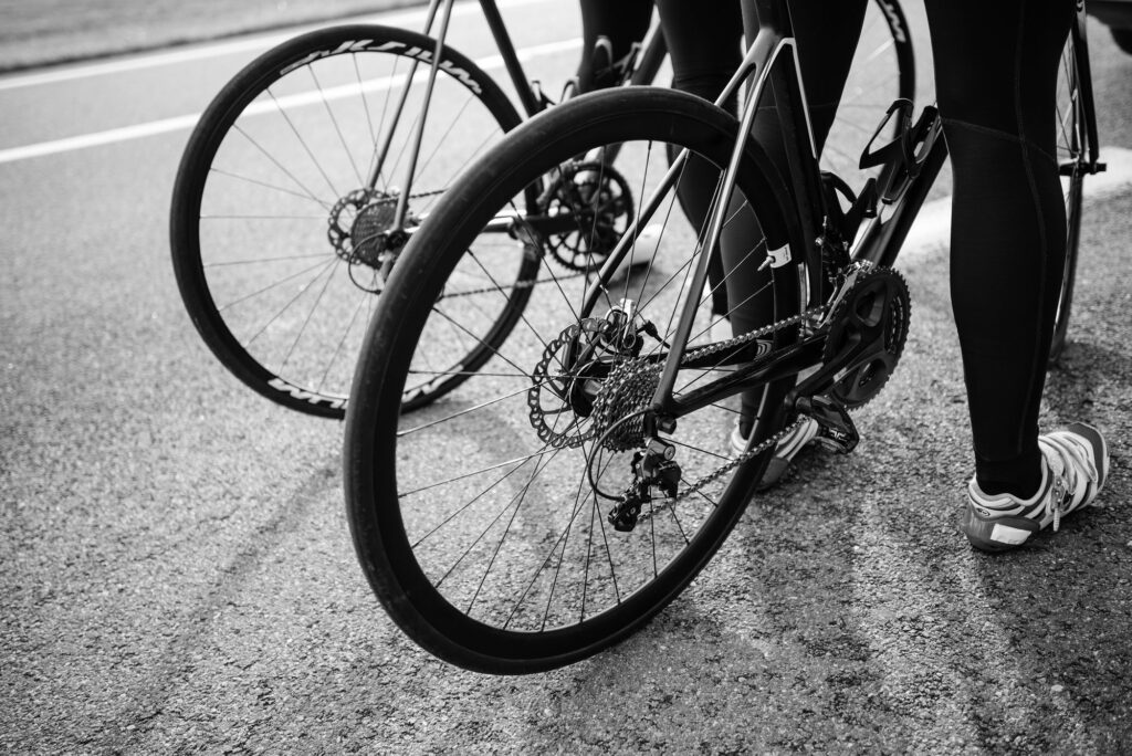Black-and-white close-up of road bike wheels and cyclists' legs on asphalt (representative image)