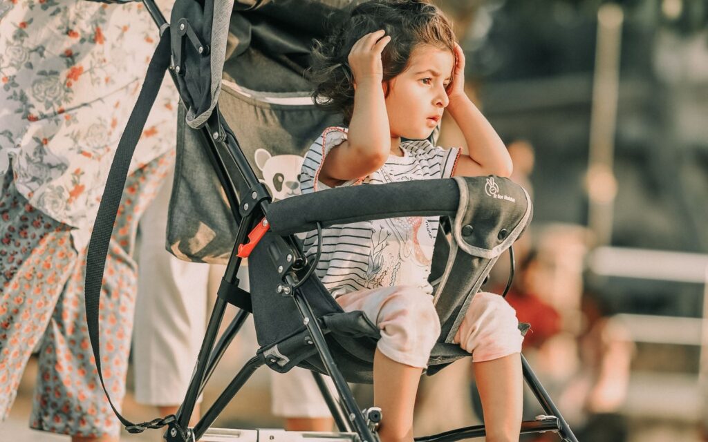 Parent pushing a toddler in a lightweight folding stroller along a paved promenade