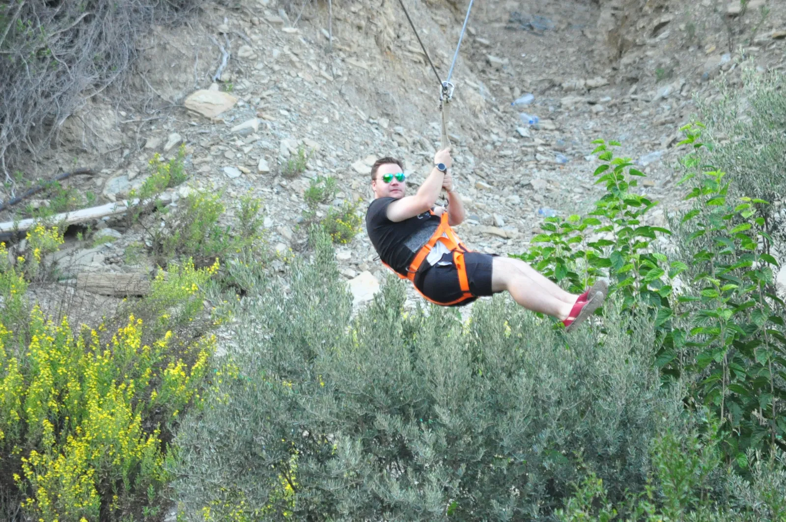 A guest riding the zipline in harness above green hillside near Köprülü Canyon
