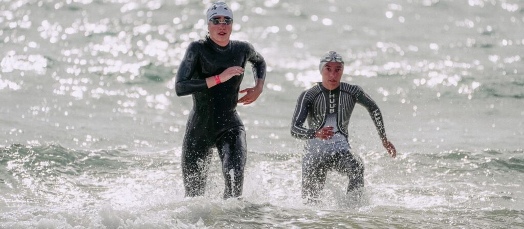 Triathletes in wetsuits running out of the sea after the swim leg, as at IRONMAN 70.3 Türkiye in Belek